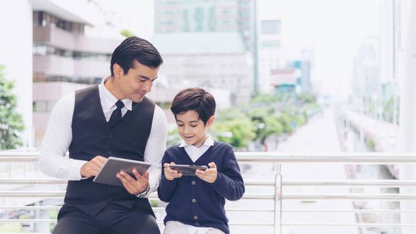 Padre e hijo jugando el teléfono inteligente del juego juntos en el distrito de negocios urbano, papá e hijo feliz concepto de familia - Foto, imagen