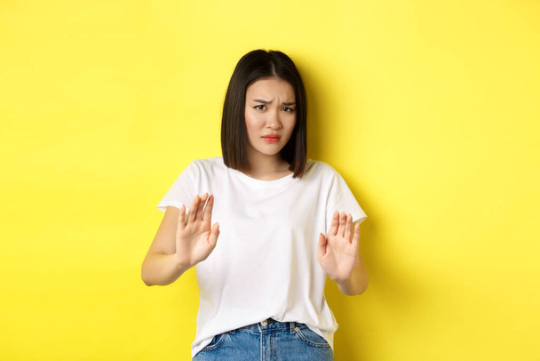 Будь ласка, ні. Азійська жінка, жертва сумирного або домашнього насильства, благаючи руки, підняті в обороні, насуплені сумно, прохаючи зупинитися, стоячи над жовтим фоном. - Фото, зображення