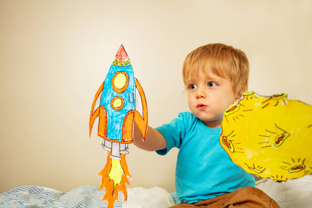 Toddler boy play astronaut holding paper rockets and planets at home with expression making sound of liftoff - Foto, immagini