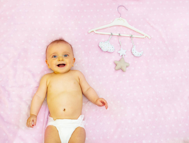 Little laughing baby girl and mobile toys hanging on a pink dotted blanket - Foto, afbeelding