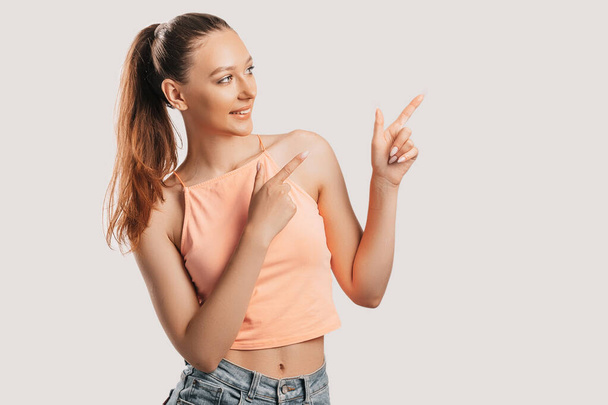 Portrait of a smiling girl pointing finger to the side at on a white isolated background. Positive woman points to an idea, a place for advertising - Valokuva, kuva