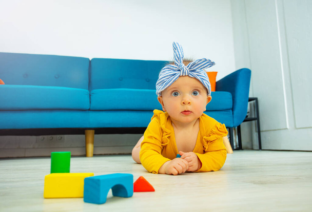 Happy baby girl play with color wooden blocks making a tower in the living room looking at camera - Photo, Image