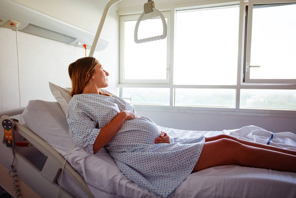 Portrait of a pregnant woman laying in hospital bed holding belly - Photo, image