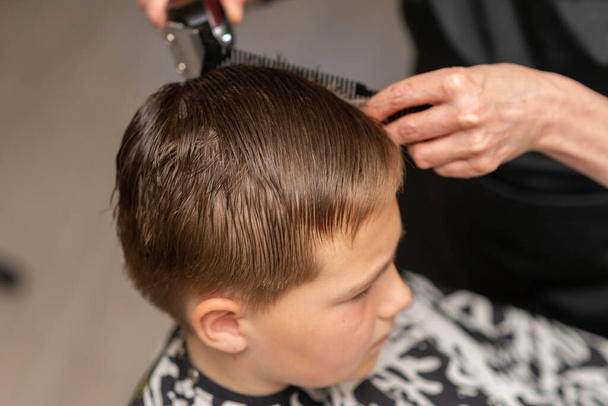 Cortar el pelo para un niño en un salón de belleza. Mano con instrumento utilizado para cortar el cabello.Manos de peluquero sosteniendo un peine y una tijera de colores.. - Foto, imagen