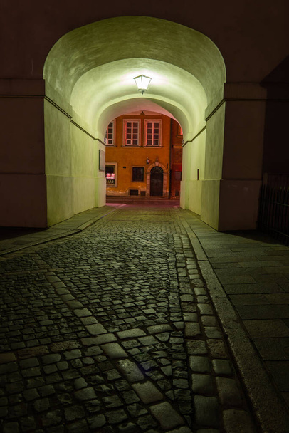 Cobblestone empty street at night with arched passage under building, illuminated with single lamp in Old Town of Warsaw, Poland. - Foto, Bild