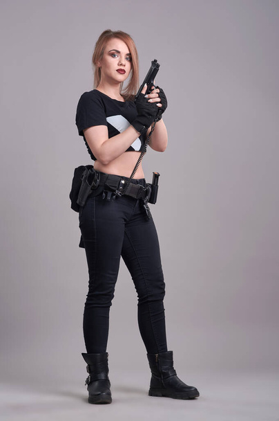 Una giovane bella donna si trova su uno sfondo grigio con una pistola in mano - Foto, immagini