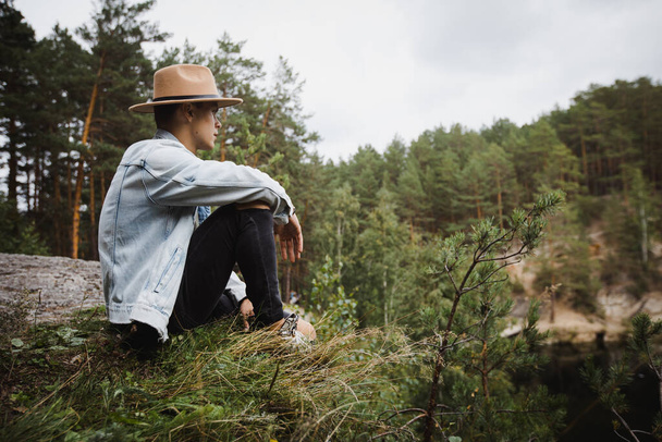 Stylowy mężczyzna siedzący na skraju skalistego zbocza wśród lasów - Zdjęcie, obraz