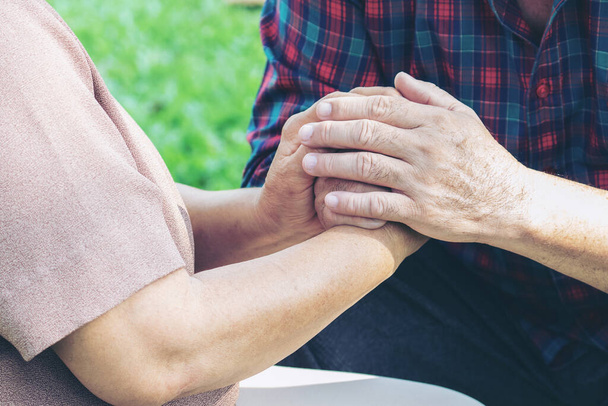 close-up de bejaarde man clasping handen van zijn vrouw met liefde in park - Foto, afbeelding