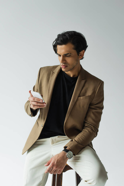 young man in blazer messaging on smartphone isolated on grey - Foto, Imagem