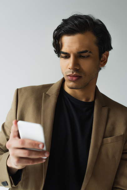 Junger Mann im Blazer textet auf Smartphone isoliert auf grau - Foto, Bild