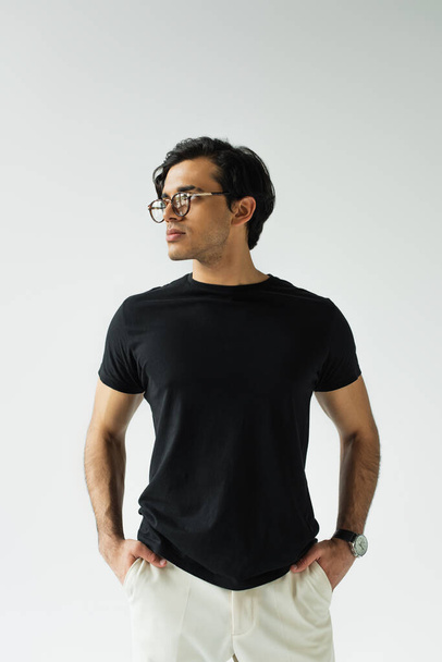 стильний чоловік в окулярах стоїть руками в кишенях ізольований на сірому
 - Фото, зображення