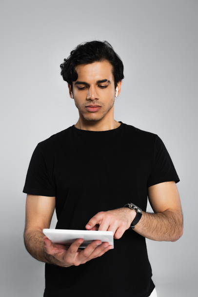 νεαρός άνδρας με μαύρο t-shirt που δείχνει το ψηφιακό δισκίο απομονώνονται σε γκρι - Φωτογραφία, εικόνα