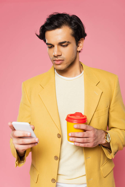 Nuori mies, joka käyttää älypuhelinta ja pitää paperimukia eristettynä vaaleanpunaiseen - Valokuva, kuva
