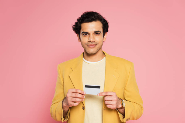 glimlachende man in gele blazer met creditcard geïsoleerd op roze - Foto, afbeelding