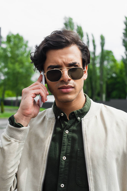 stylish young man in sunglasses and bomber jacket talking on mobile phone  - Photo, Image