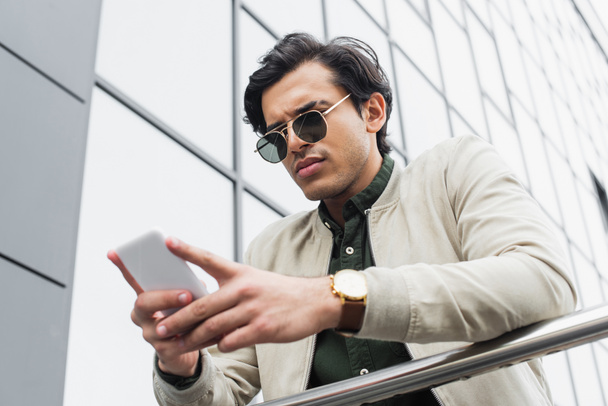 low angle view of stylish young man in sunglasses chatting on mobile phone  - Photo, Image