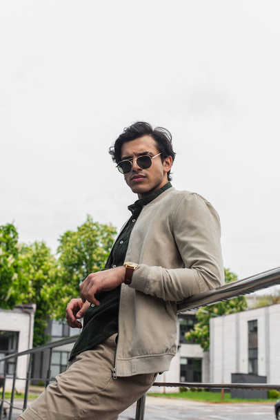 young man in stylish sunglasses and bomber jacket posing outside - Photo, image