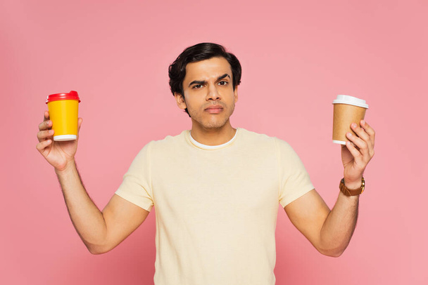 confused man choosing paper cups isolated on pink - Foto, Imagem