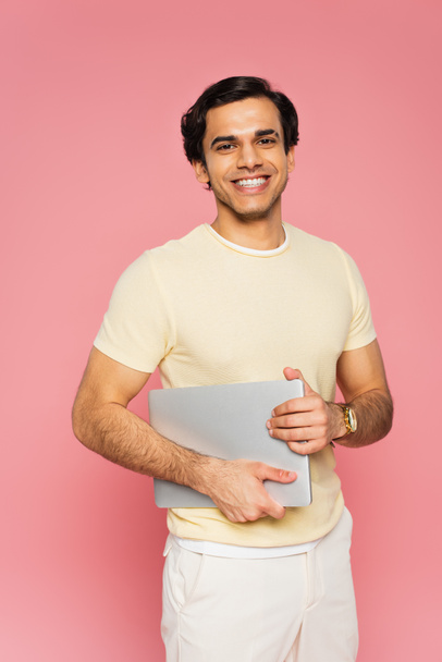 cheerful freelancer holding laptop isolated on pink - 写真・画像