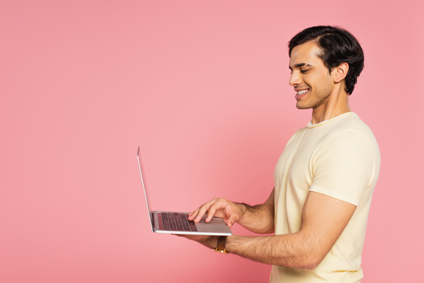 cheerful freelancer typing on laptop isolated on pink - Fotó, kép