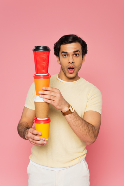 shocked young man holding stacked paper cups isolated on pink  - Φωτογραφία, εικόνα