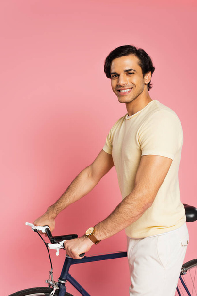 Ευτυχισμένος νεαρός άνδρας στέκεται κοντά ποδήλατο σε ροζ - Φωτογραφία, εικόνα