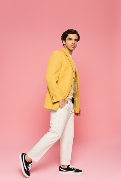full length of young man in trendy yellow blazer posing with hand in pocket isolated on pink  - Photo, Image