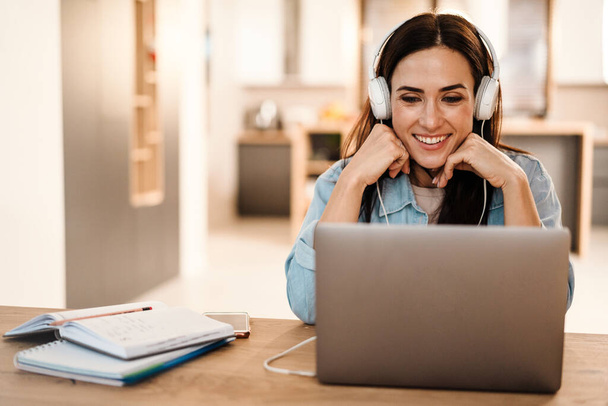 Happy beautiful woman in headphones smiling while using laptop at home - Foto, Imagen