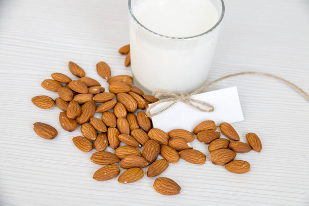Almond Milk with Almond Nuts on White Wooden Table. White Card with Burlap Strap. A place for Text. - Fotoğraf, Görsel