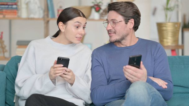 Smíšené rasy pár pomocí smartphonu a mluvení při sezení doma  - Fotografie, Obrázek