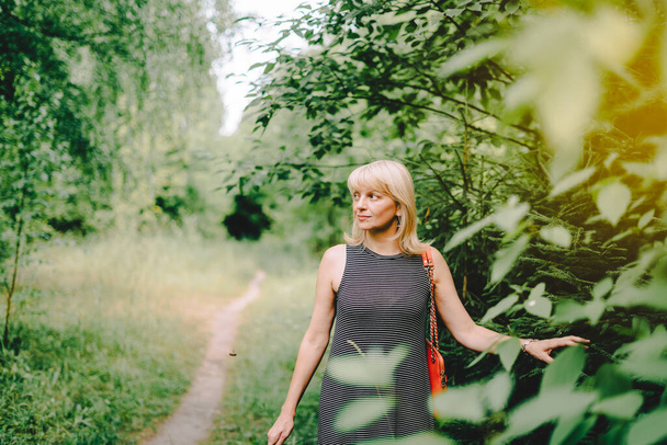 Sommerporträt einer erwachsenen blonden Frau in der Nähe der Bäume an einem sonnigen Tag im Park. - Foto, Bild