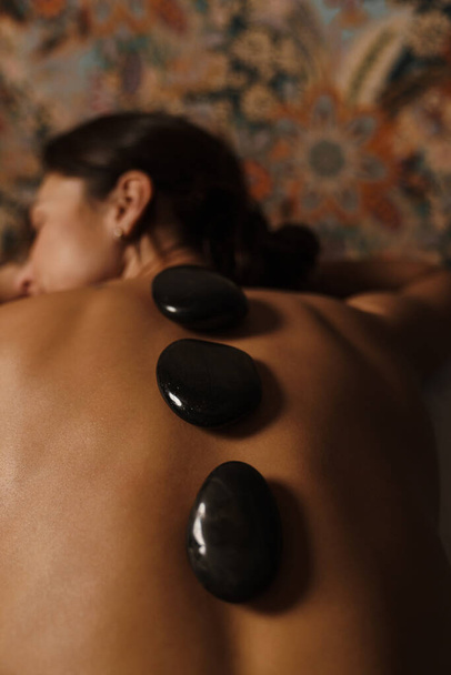White relaxed shirtless woman lying during spa treatment with stones indoors - Foto, Bild