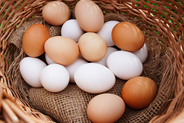 Orgaaninen maalaismainen valkoinen ja ruskea kananmunat lähikuva luonnollisella liinalla korissa ja keltainen pieni kana, luomuruokaa kylästä. - Valokuva, kuva