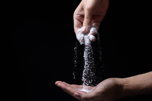 Salt on a black background. Hand sprinkles salt on hand on dark background - Foto, Imagen