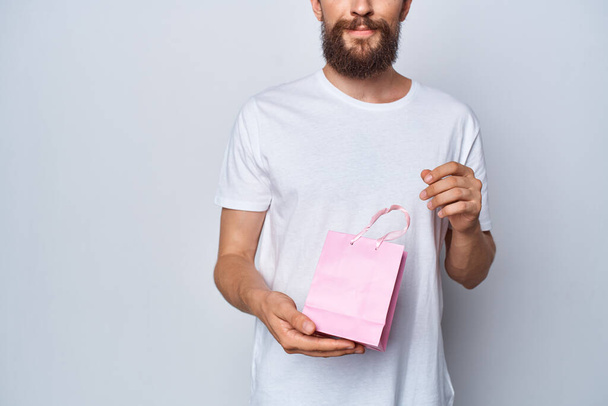 a man in a white t-shirt holding a pink package gift holiday present - Фото, зображення