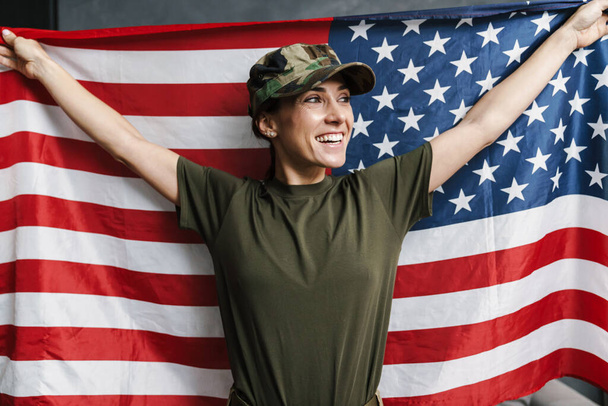 Happy soldier woman smiling while posing with american flag indoors - Fotoğraf, Görsel
