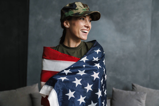 Happy soldier woman smiling while posing with american flag indoors - Foto, imagen