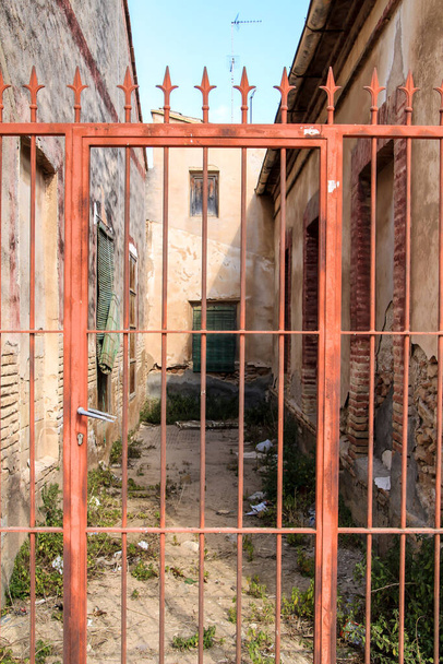 スペインのムルシア州のロス・アルカサレス村に赤い錬鉄製の門を持つ放棄された家 - 写真・画像