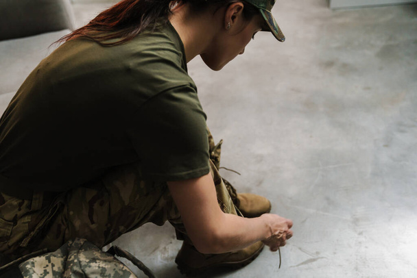 Soldier woman tying her shoe laces while sitting on couch indoors - Foto, imagen