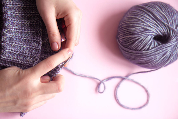 Mãos femininas com agulhas de tricô para tricotar camisola violeta de lã e emaranhado de fio de lã no fundo rosa. Mulher a tricotar roupas de lã. Disparo aéreo. Fechar - Foto, Imagem