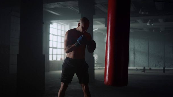 Boxer pratique coups de pied sur sac de boxe dans la salle de gym. Guy sac de sport de boxe en gants - Photo, image