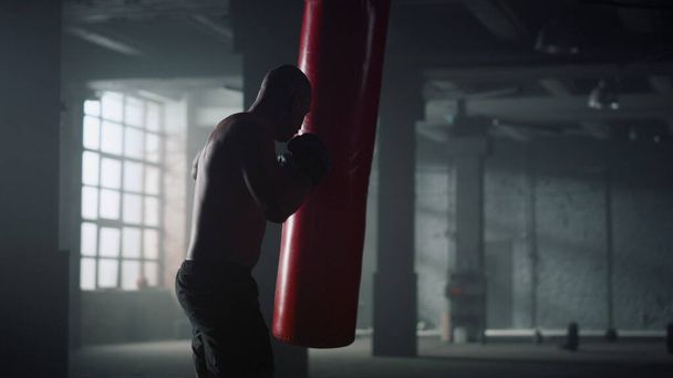 Un athlète frappe un sac de boxe avec des gants. Guy travailler sur des coups sur le sac de sport - Photo, image
