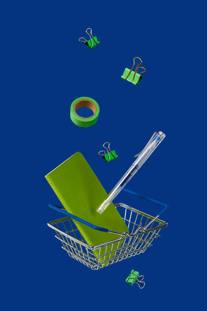 Stationery office supplies with shopping cart levitate on blue background - Photo, Image