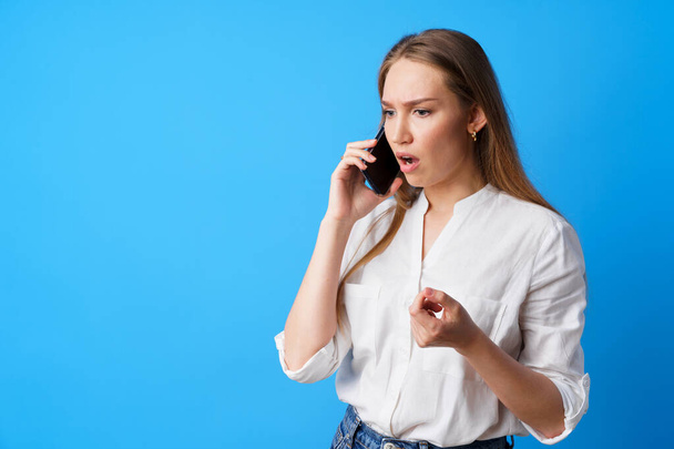 Unhappy woman talking on the phone stressed with bad news, blue background - Photo, image