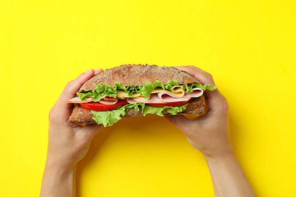 Female hands hold ciabatta sandwich on yellow background - Fotoğraf, Görsel