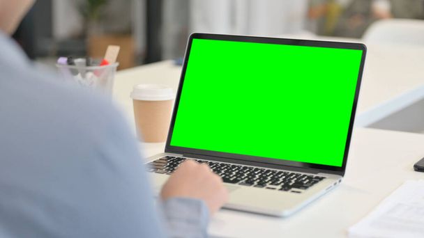 Vista trasera de la mujer africana usando el ordenador portátil con la pantalla dominante verde del croma - Foto, imagen