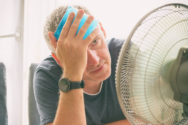 Az ember szenved a hő otthon, és megpróbál lehűlni a ventilátor - Fotó, kép