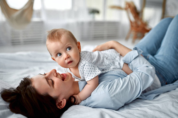 Loving mom carying of her newborn baby at home.Mom and baby boy playing in sunny bedroom. Parent and little kid relaxing at home. Family having fun together. Childcare, maternity concept. - Foto, Imagem