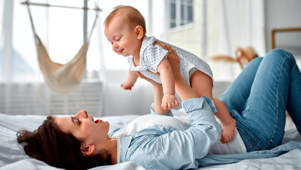Loving mom carying of her newborn baby at home.Mom and baby boy playing in sunny bedroom. Parent and little kid relaxing at home. Family having fun together. Childcare, maternity concept. - Foto, imagen