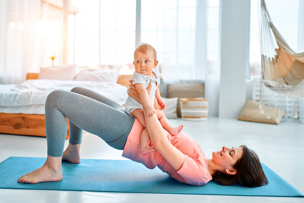 A sports mother is engaged with the child in fitness and yoga at home. The concept of sports, motherhood and an active lifestyle. Young woman in sports training with her child. - Foto, Bild